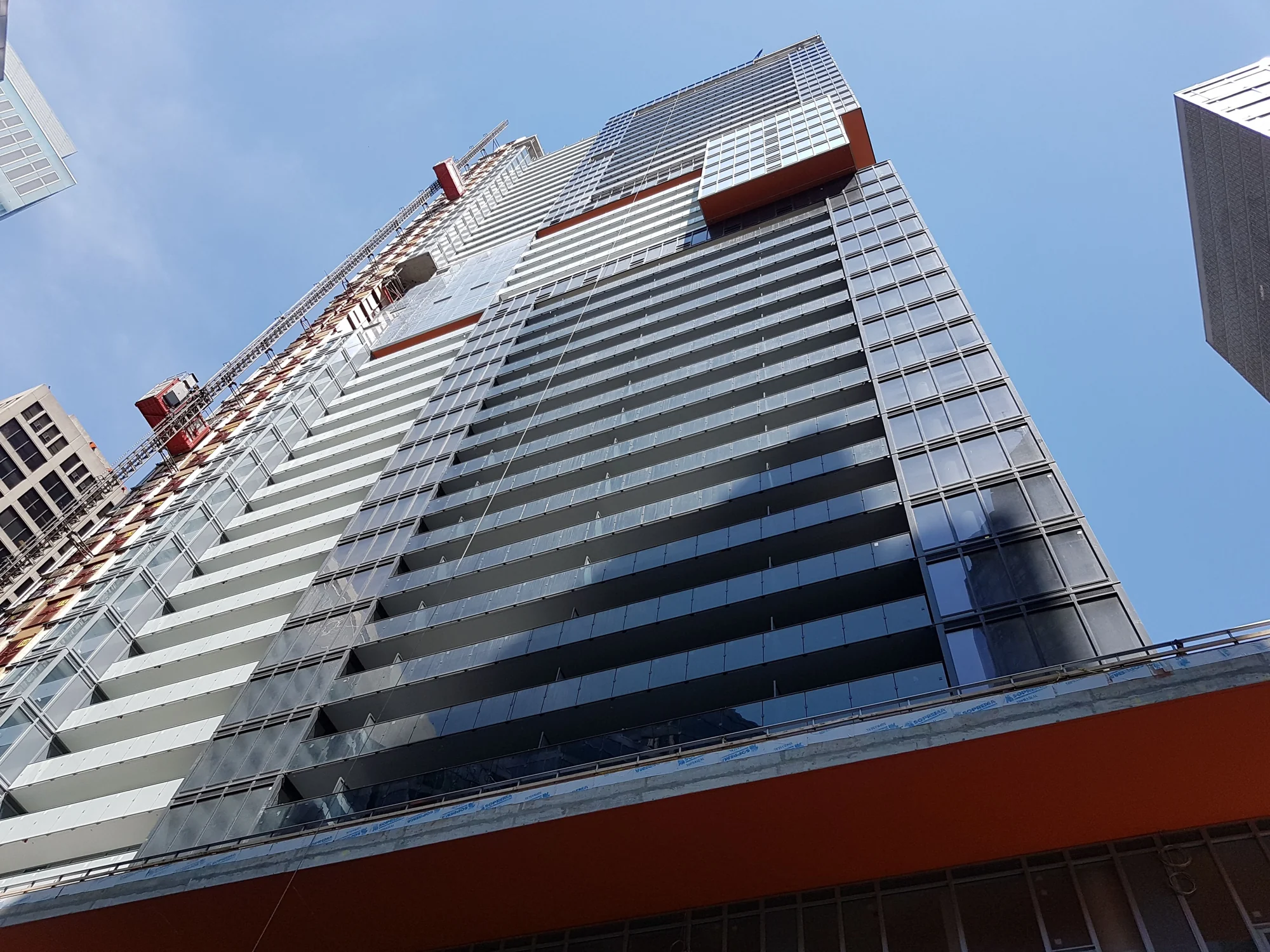 Looking up at a high-rise facade with glass balcony panels and copper-coloured architectural bands