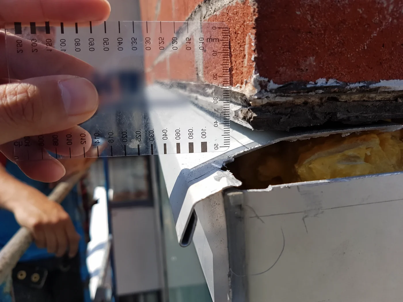 Close-up measurement of the exposed interface between masonry, insulation and window head flashing